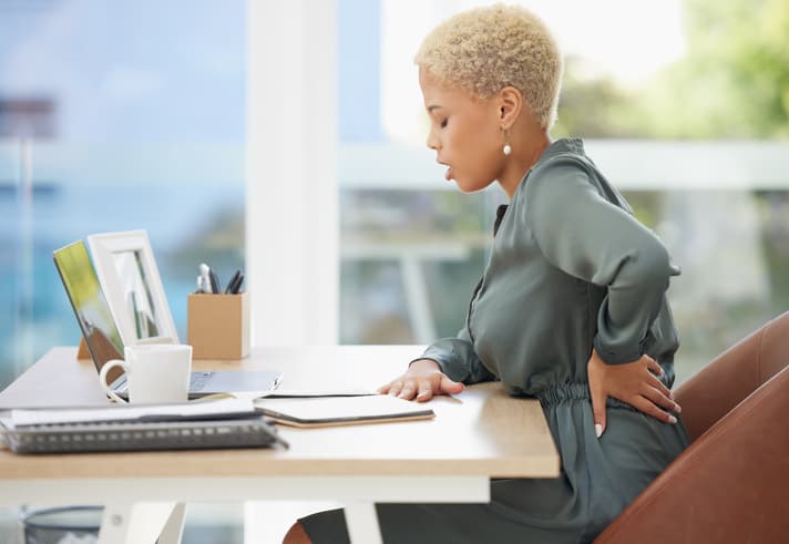 Businesswoman sitting at her desk experiencing lower back pain