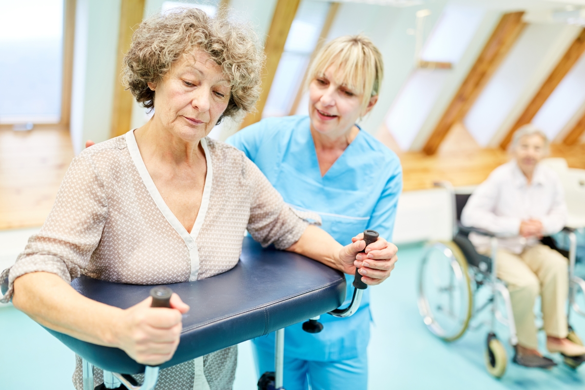 Therapist helps senior citizen with walker learning to walk in rehab clinic