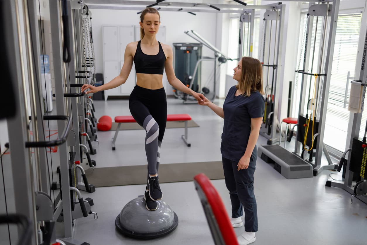 Woman performing balance exercise with trainer in rehabilitation gym