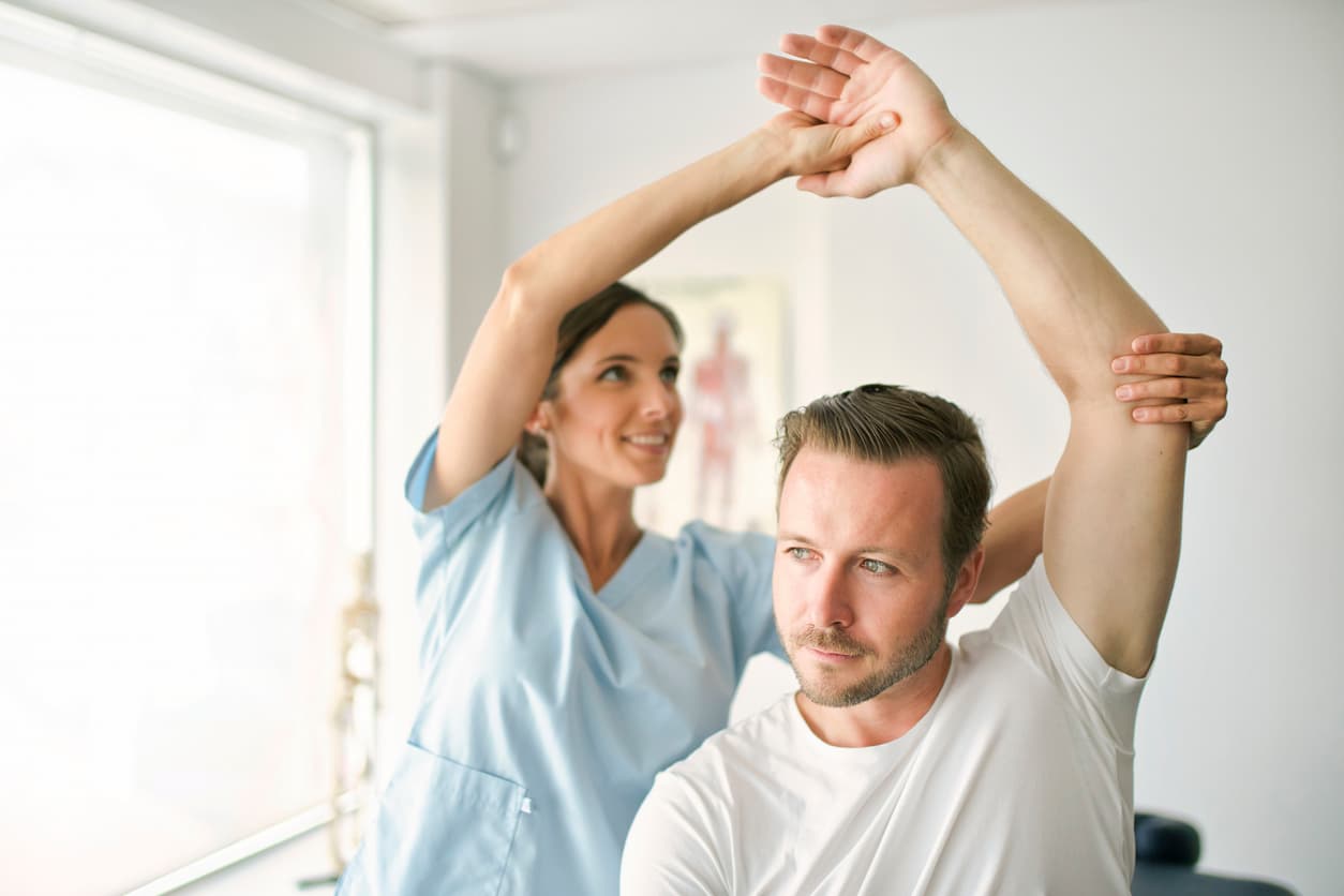 Physical therapist assisting man with shoulder mobility stretch