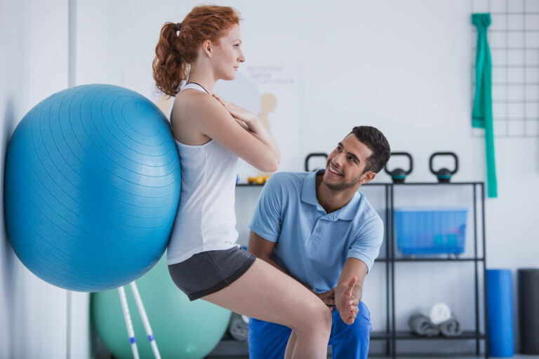 a-male-in-home-physical-therapist-helping-an-exercise-therapy-patient-roll-on-a-blue-ball