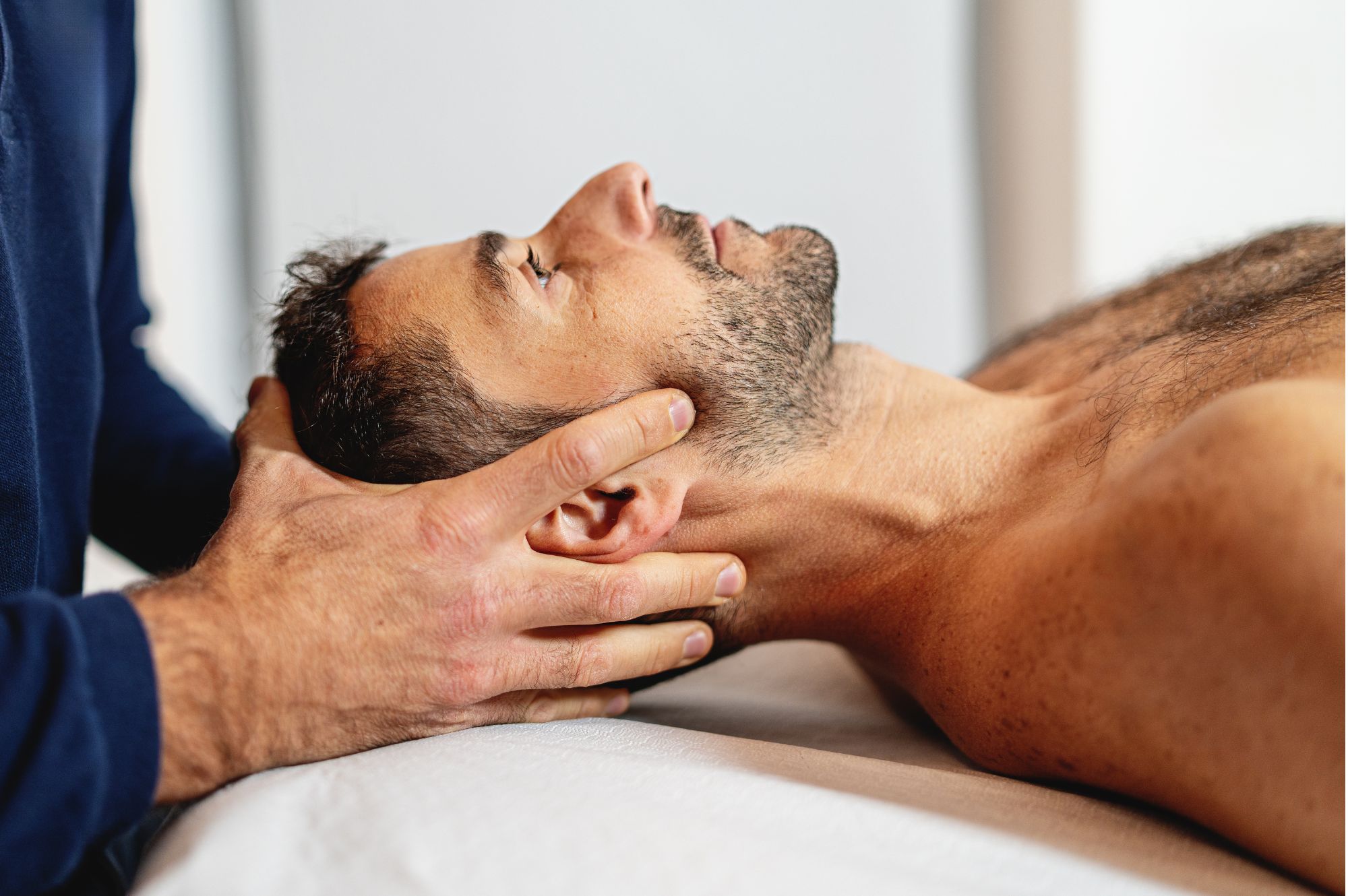 A healthcare practitioner supports a man’s head and neck as he lies on a treatment table during a hands-on therapy session.