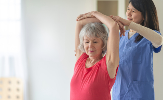 An older adult practices overhead mobility with therapist support during exercise therapy in Edmonton