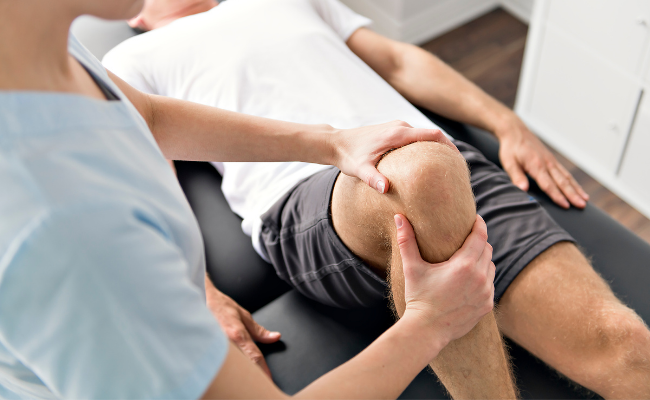 Physiotherapist assessing a patient’s knee during an in-home appointment