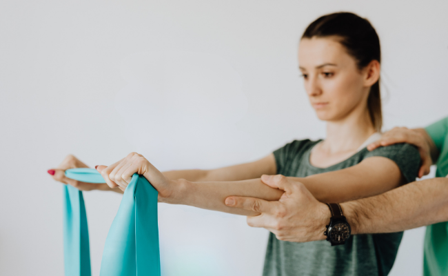 Physiotherapist guiding a patient through a resistance band arm exercise at home