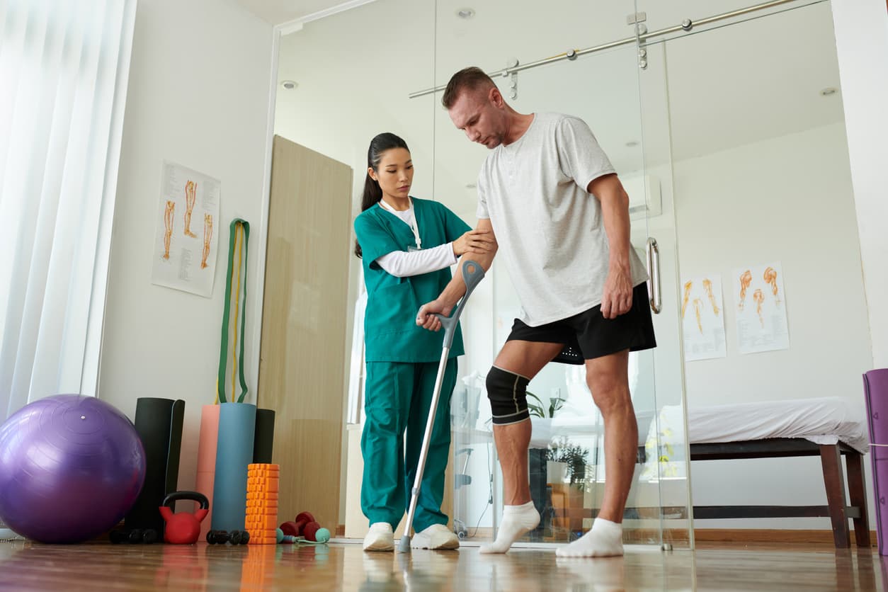 Physical therapist assisting man with knee rehabilitation and crutch walking exercise