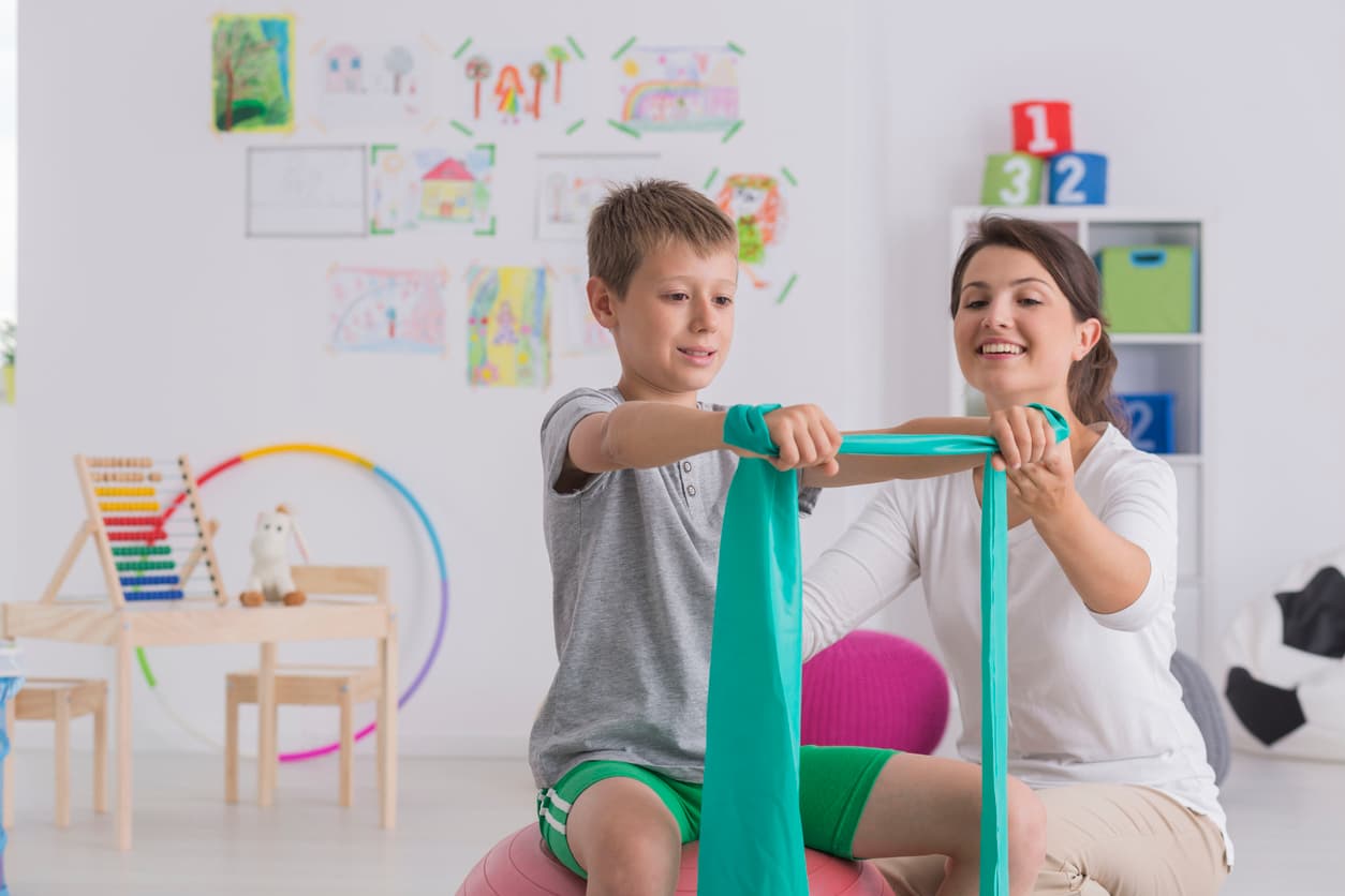 Child doing resistance band exercise with therapist during pediatric physical therapy session