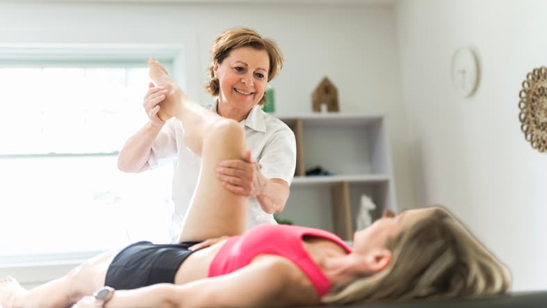 Physical therapist assisting a woman with leg rehabilitation exercises