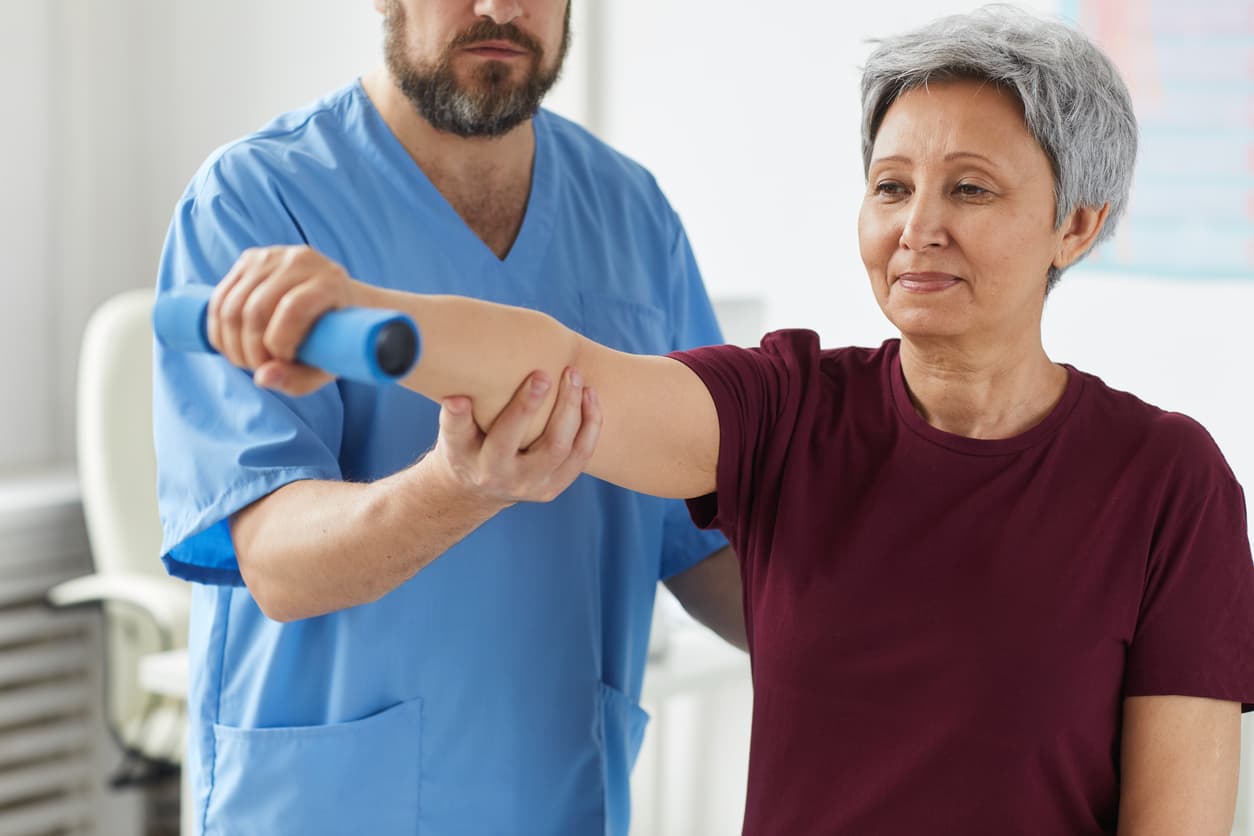 Senior woman performing arm rehabilitation exercise with physiotherapist