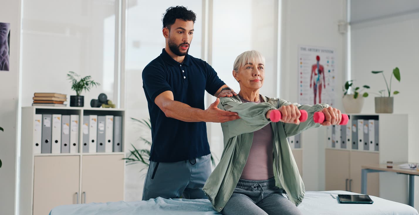 Senior woman doing light dumbbell exercises with physiotherapist